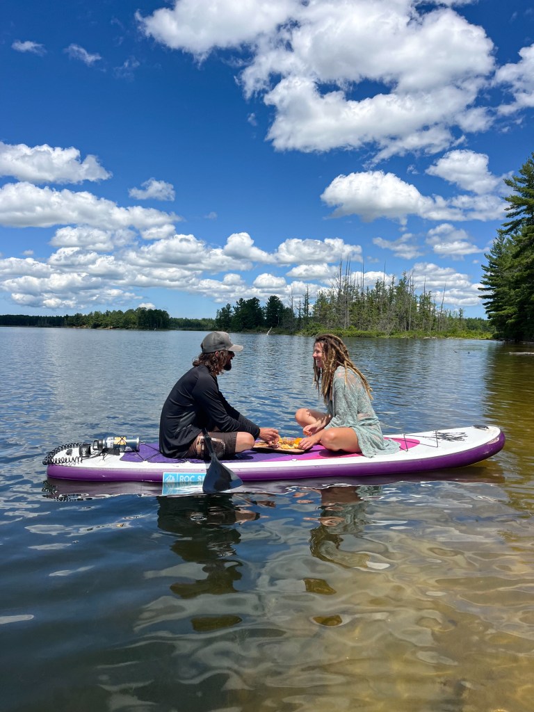 People on a lake in Michigan having a paddle board date with snacks and a good view by Adventurous Leila.