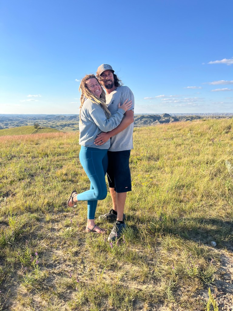 A photo of a cute couple taking a photo on a hike at Theodore Roosevelt national Park. By Adventurous Leila.